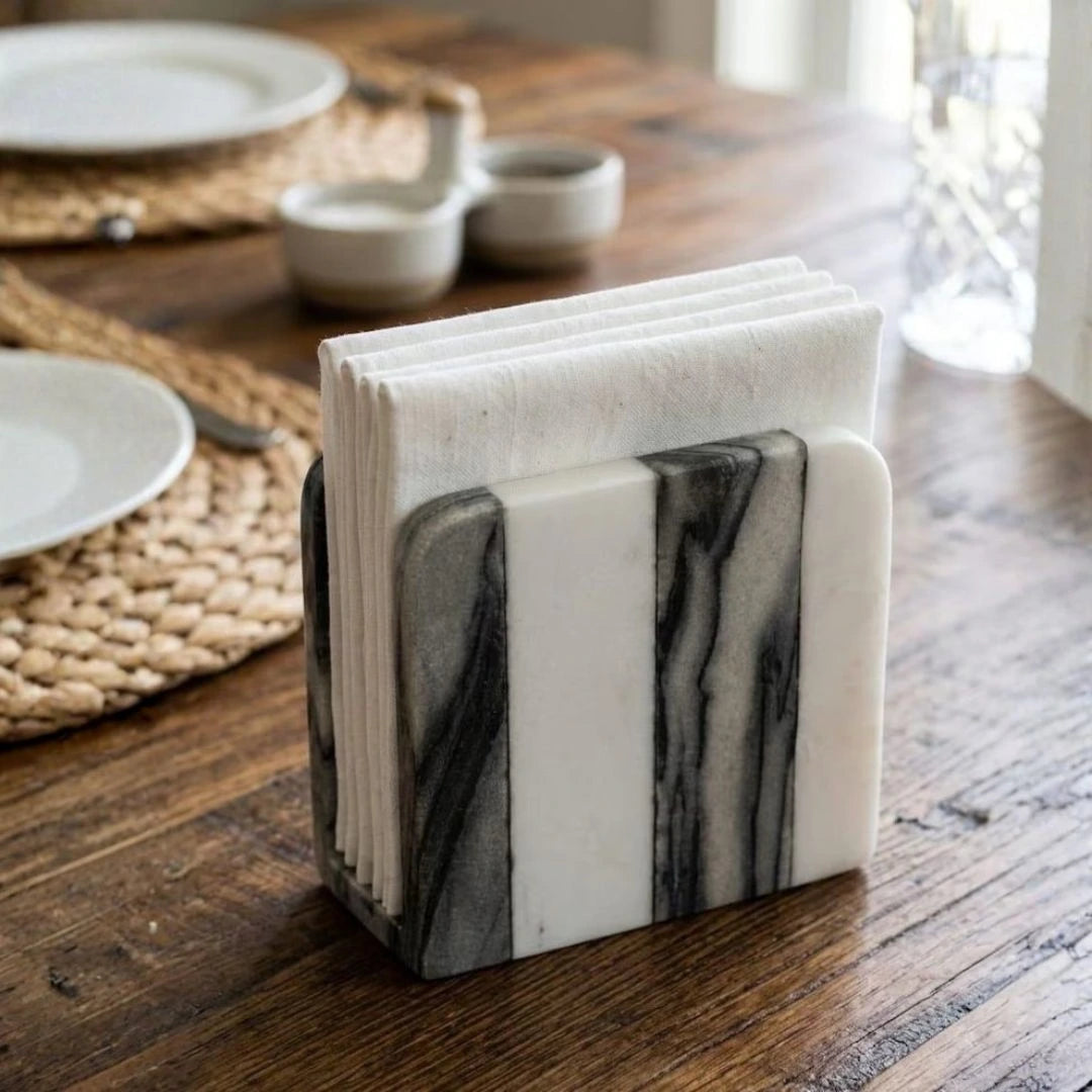 White and gray natural marble napkin holder displayed on a wooden table with neatly folded fabric napkins.