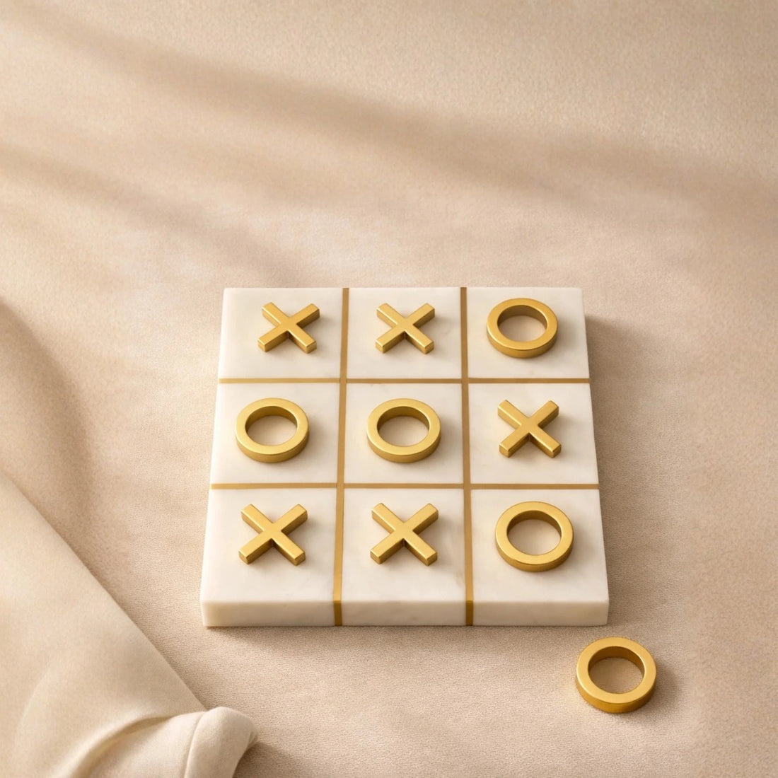 Luxury white marble tic tac toe game with gold inlay grid and metallic X and O pieces on a neutral background