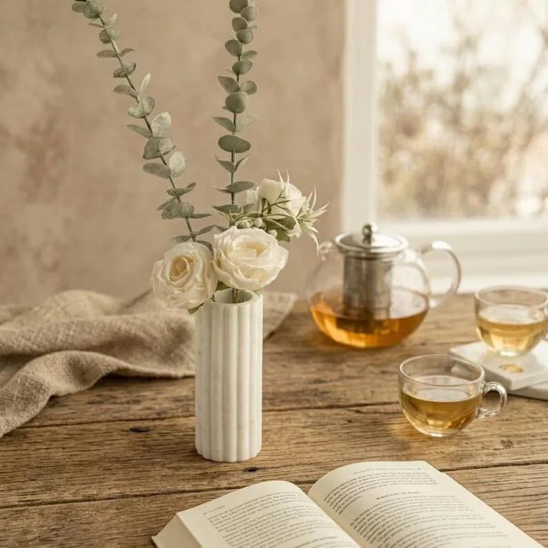 White fluted marble Vase standing on a rustic wooden table with a minimalist, warm home decor setting.
