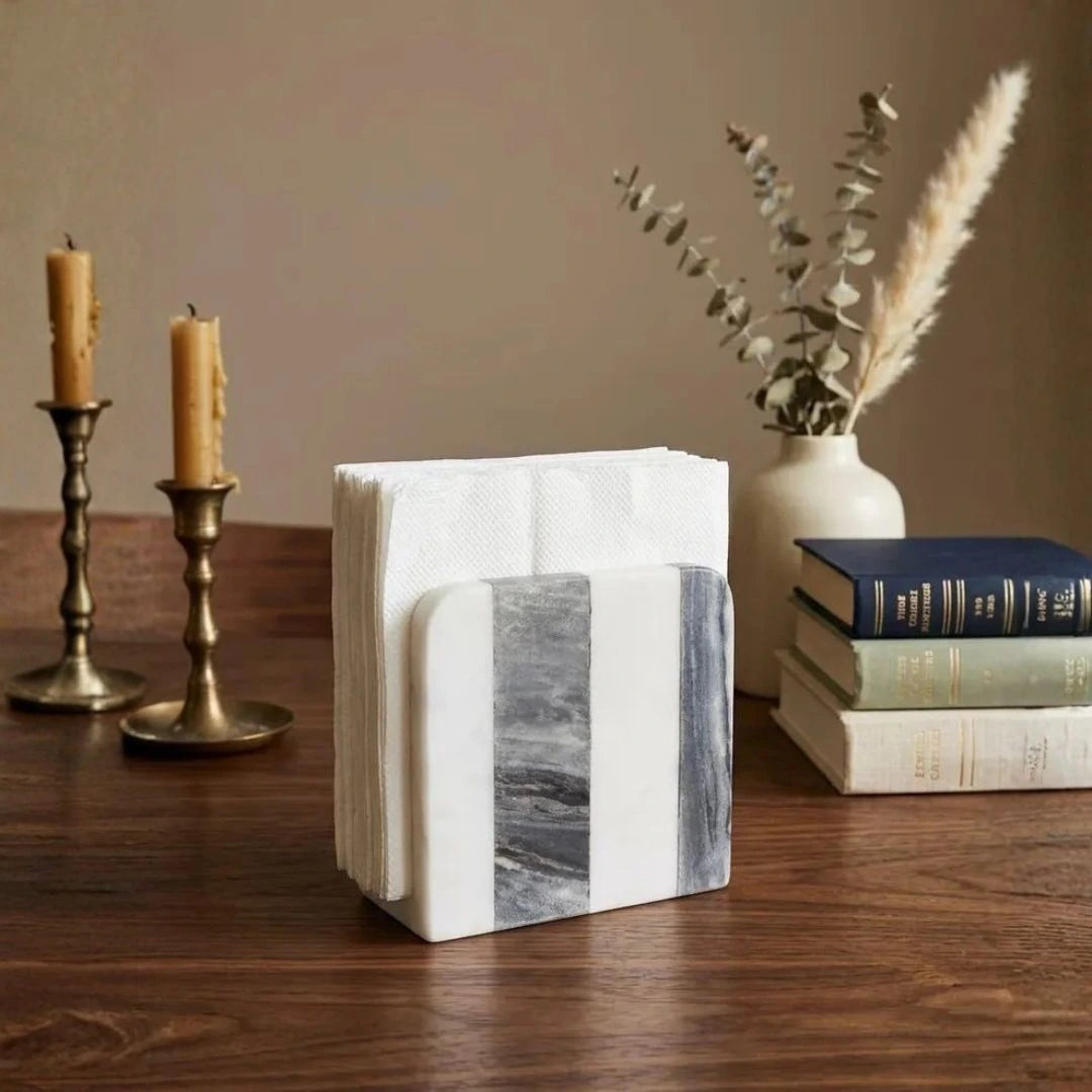 White and gray natural marble napkin holder displayed on a wooden table with neatly folded fabric napkins.